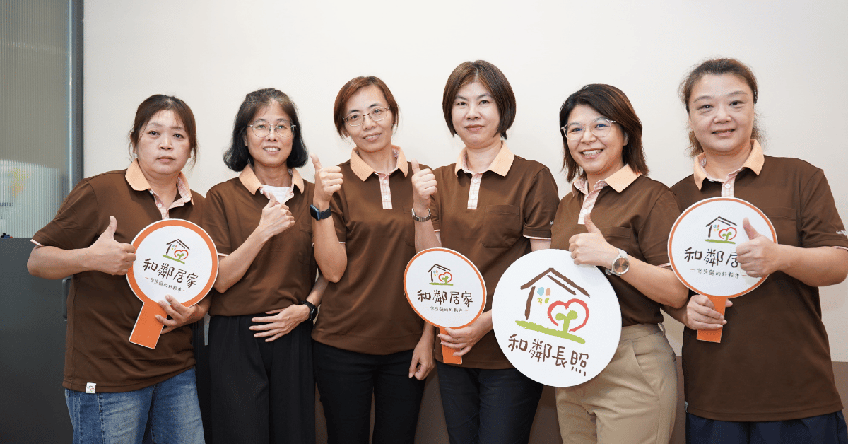 和鄰長照六位團隊成員穿著棕色制服合影，手持「和鄰居家」與「和鄰長照」標誌牌，並比出讚的手勢。